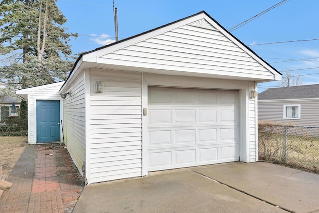 detached garage featuring concrete driveway and fence