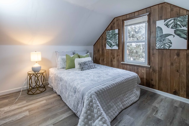 bedroom featuring vaulted ceiling, wood walls, wood finished floors, and baseboards