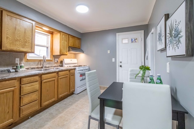 kitchen with light tile patterned floors, tasteful backsplash, white gas range, a sink, and under cabinet range hood