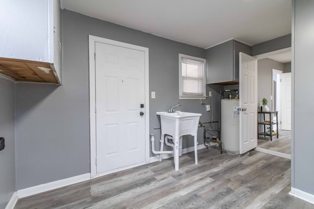 washroom featuring water heater, a sink, wood finished floors, and baseboards