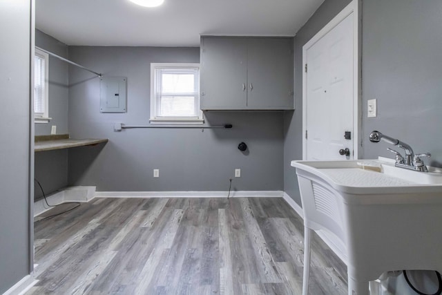 laundry room featuring electric panel, a sink, baseboards, and wood finished floors