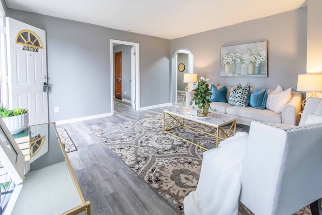 living area featuring arched walkways, wood finished floors, and baseboards