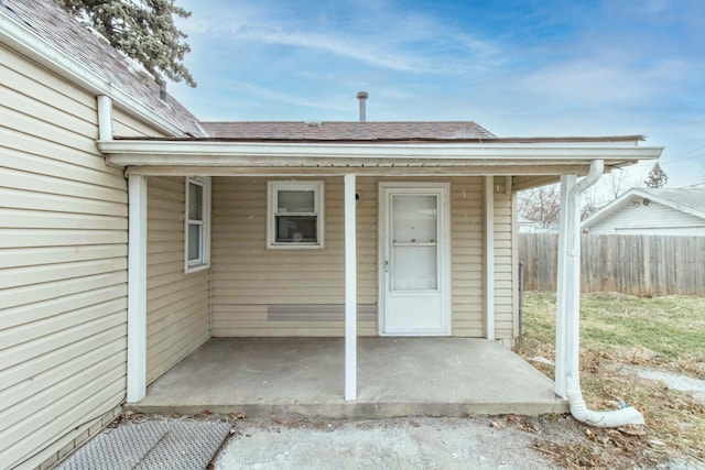 view of exterior entry featuring fence, a carport, and roof with shingles