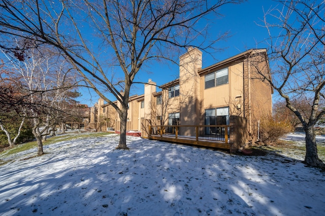 snow covered property with a wooden deck and a chimney