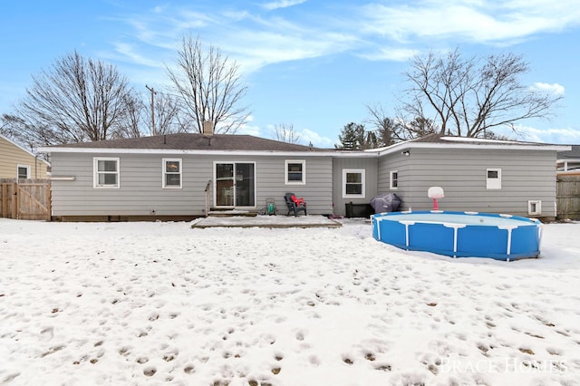 snow covered house featuring a chimney, fence, and an outdoor pool