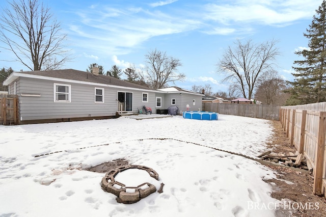 snow covered house with entry steps, a fenced backyard, and a chimney