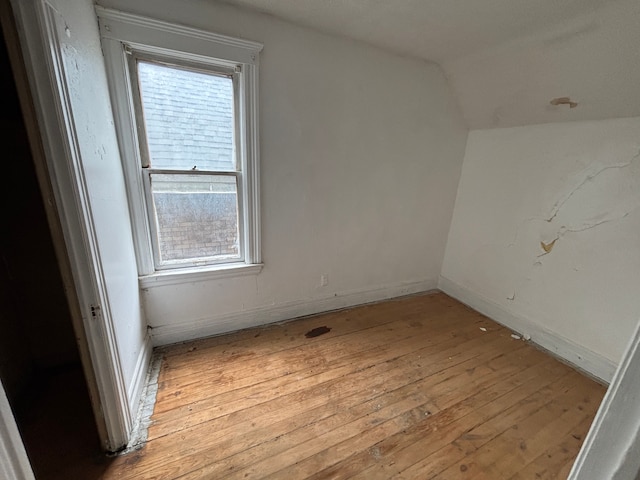 empty room featuring lofted ceiling, light wood-style floors, and baseboards