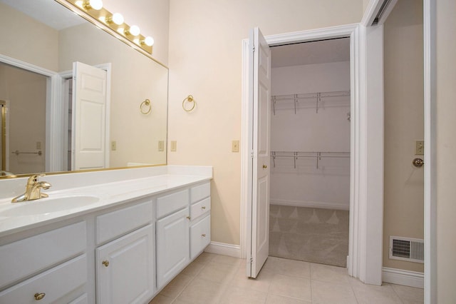 bathroom with tile patterned flooring, vanity, visible vents, baseboards, and a spacious closet