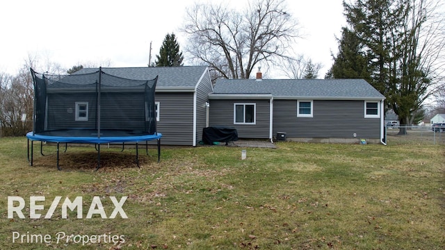 back of property featuring a lawn, a chimney, roof with shingles, a trampoline, and fence