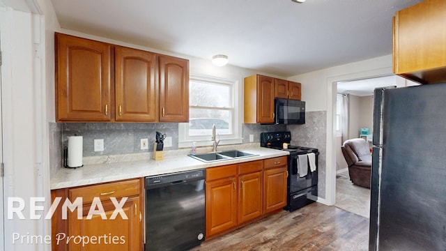 kitchen with brown cabinets, light countertops, a sink, wood finished floors, and black appliances