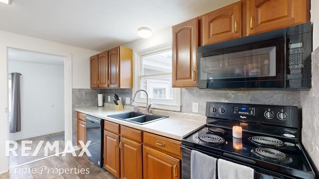 kitchen with decorative backsplash, brown cabinets, light countertops, black appliances, and a sink