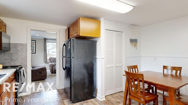 kitchen with decorative backsplash, light wood-type flooring, light countertops, and black appliances