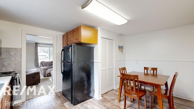 kitchen with black appliances, light countertops, light wood-style flooring, and baseboards