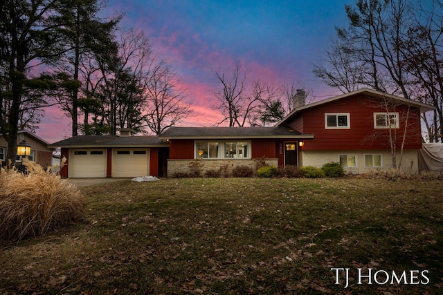 split level home with an attached garage, driveway, a chimney, and a front lawn