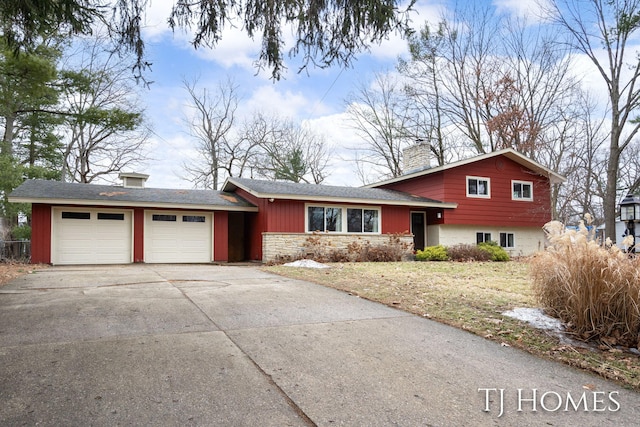 tri-level home with driveway, stone siding, a chimney, and an attached garage