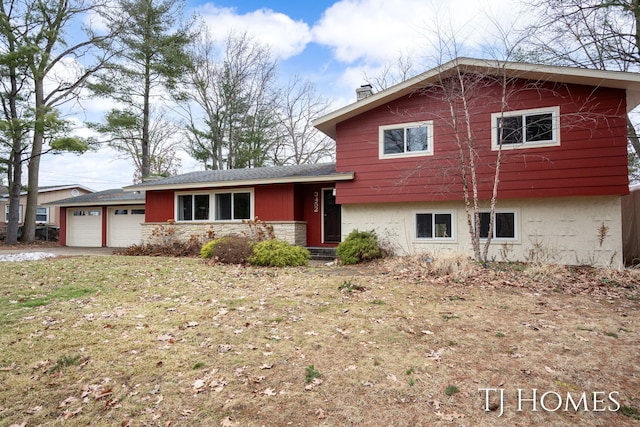 split level home featuring a front yard, stone siding, a chimney, and an attached garage