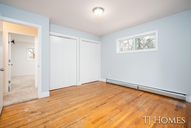 unfurnished bedroom with hardwood / wood-style flooring, baseboards, baseboard heating, and multiple closets