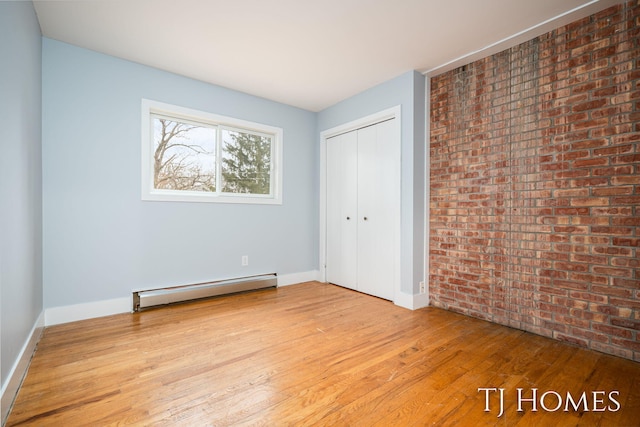 unfurnished bedroom with a baseboard heating unit, brick wall, baseboards, a closet, and hardwood / wood-style floors