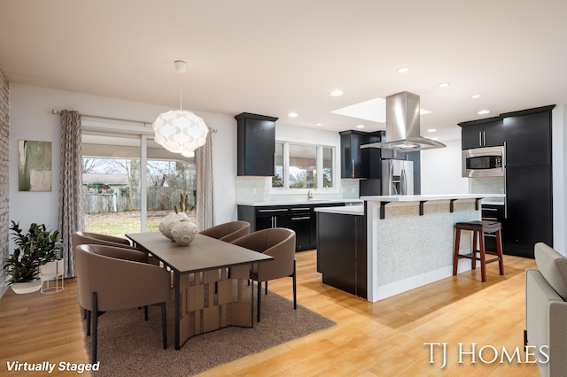 kitchen featuring a breakfast bar, stainless steel appliances, island range hood, light countertops, and dark cabinets