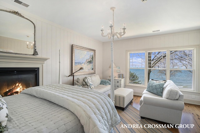 6059 Lakeshore Dr, West Olive, MI 49460 - bedroom with wood-type flooring, visible vents, a chandelier, and a glass covered fireplace