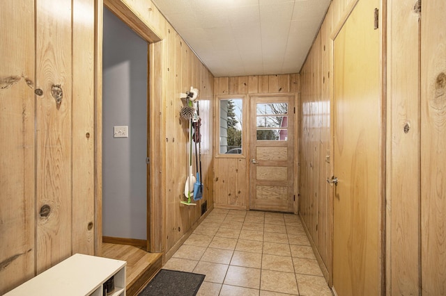 doorway to outside featuring light tile patterned floors, baseboards, and wooden walls