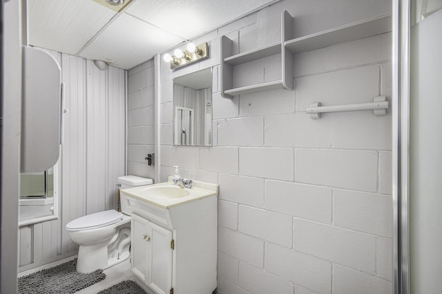 bathroom featuring concrete block wall, vanity, and toilet