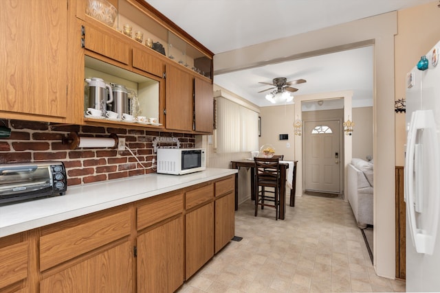 kitchen featuring white appliances, a toaster, brown cabinetry, a ceiling fan, and light countertops