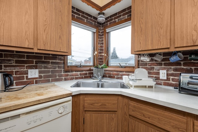 kitchen featuring brick wall, brown cabinetry, white dishwasher, and a sink