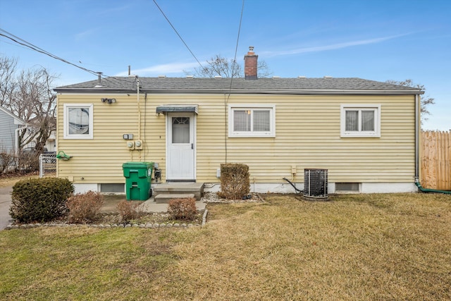 back of house with a lawn, a chimney, roof with shingles, fence, and central air condition unit