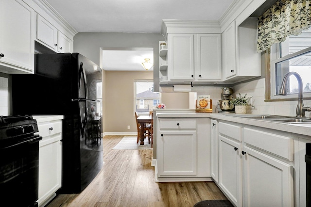 kitchen featuring black range with gas cooktop, light wood-type flooring, a sink, and white cabinetry