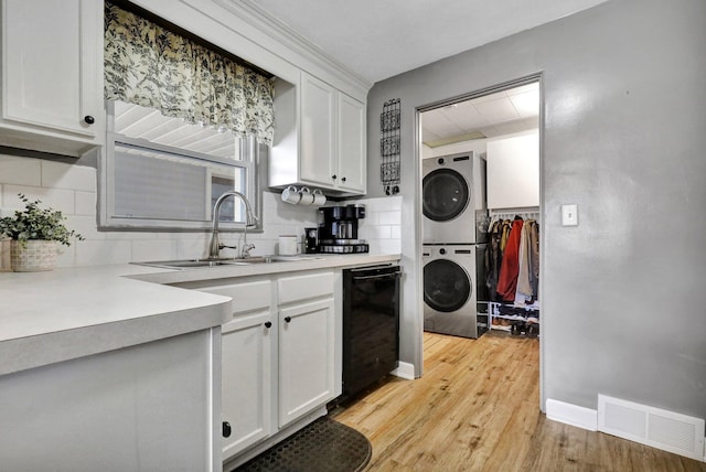 kitchen featuring light wood-style flooring, a sink, visible vents, stacked washing maching and dryer, and backsplash