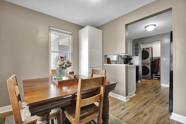 dining space with stacked washer / drying machine, light wood-style flooring, and baseboards