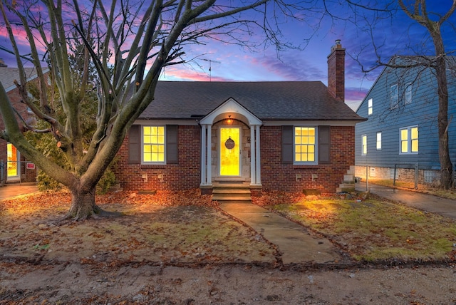 bungalow featuring brick siding, a chimney, and roof with shingles