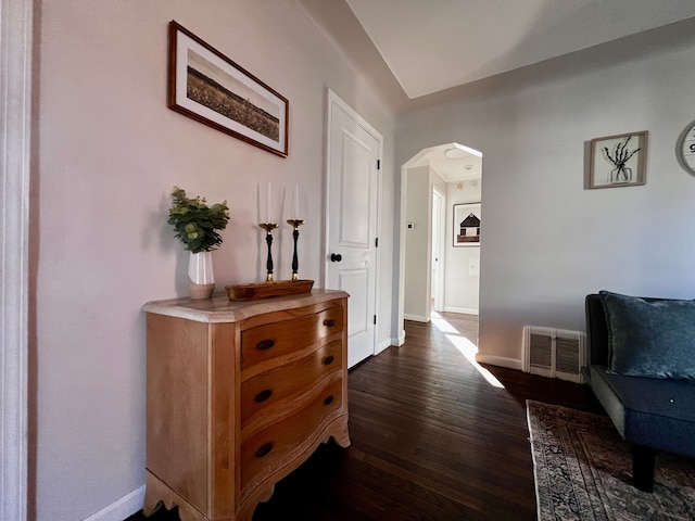 hall with dark wood-type flooring, arched walkways, visible vents, and baseboards