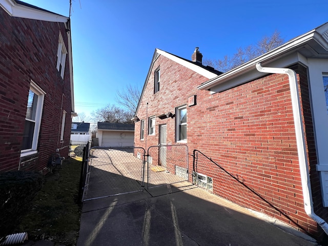 view of side of property featuring brick siding, an outdoor structure, fence, and a gate