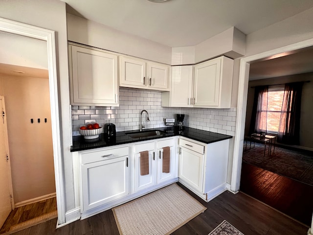 kitchen featuring tasteful backsplash, white cabinets, dark countertops, dark wood-style flooring, and a sink