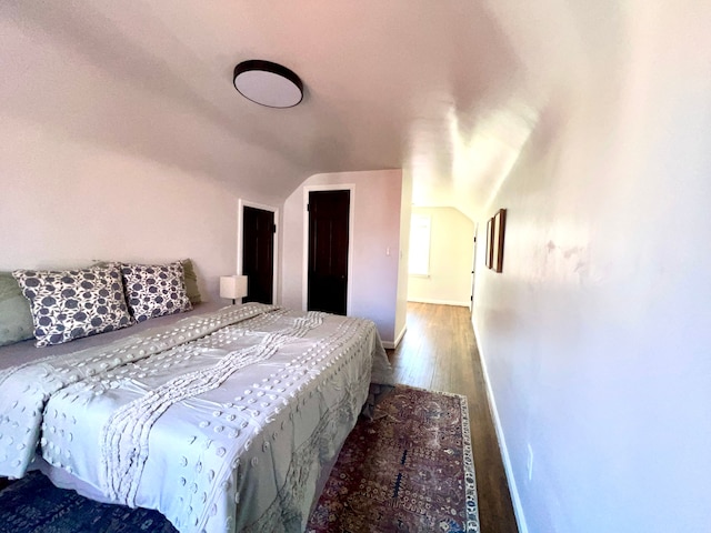 bedroom with baseboards, vaulted ceiling, and wood finished floors