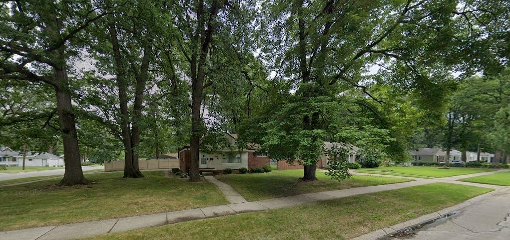 view of property hidden behind natural elements featuring a front lawn and a residential view