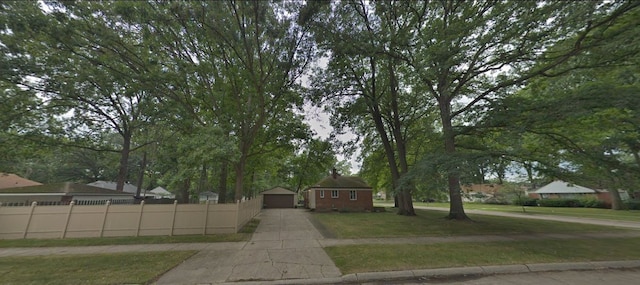 view of property hidden behind natural elements featuring a garage, fence, a front lawn, and an outbuilding