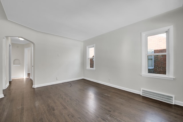 spare room with dark wood-type flooring, arched walkways, visible vents, and baseboards