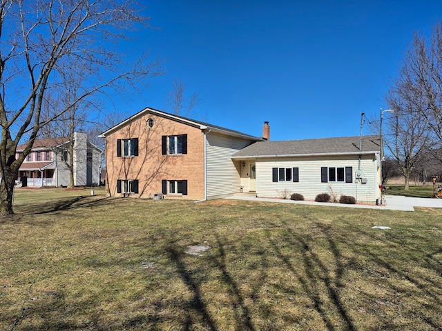 back of property featuring brick siding, a yard, and a chimney