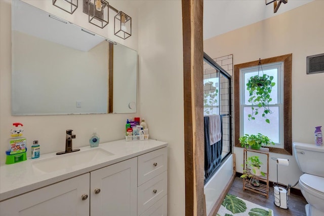 bathroom featuring visible vents, toilet, enclosed tub / shower combo, vanity, and wood finished floors