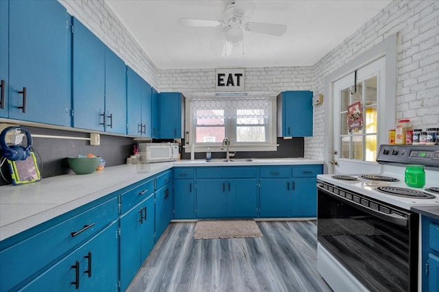 kitchen with blue cabinets, white appliances, a sink, and brick wall