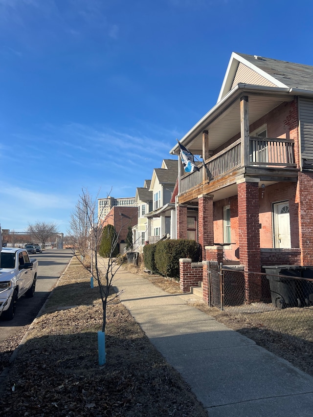 view of side of property with a balcony, fence, brick siding, and a residential view