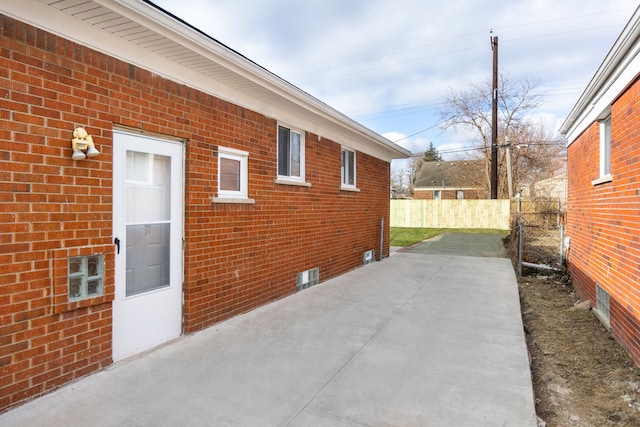 view of side of home with a patio, brick siding, and fence