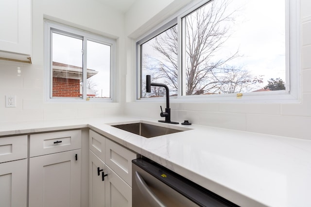 kitchen featuring light stone counters, a sink, white cabinetry, and a healthy amount of sunlight