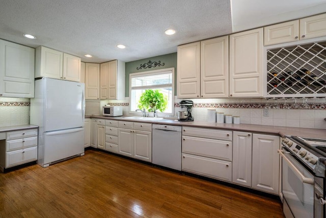 kitchen with dark wood-style floors, white appliances, a sink, and decorative backsplash