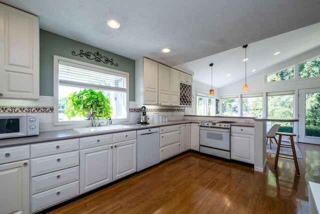 kitchen with white appliances, lofted ceiling, dark wood-style flooring, a peninsula, and white cabinetry