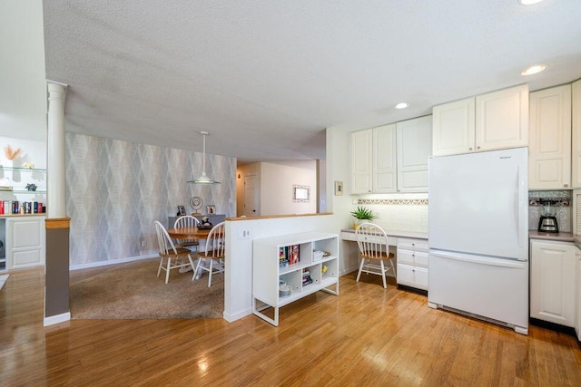 kitchen with light wood finished floors, white cabinetry, built in study area, and freestanding refrigerator