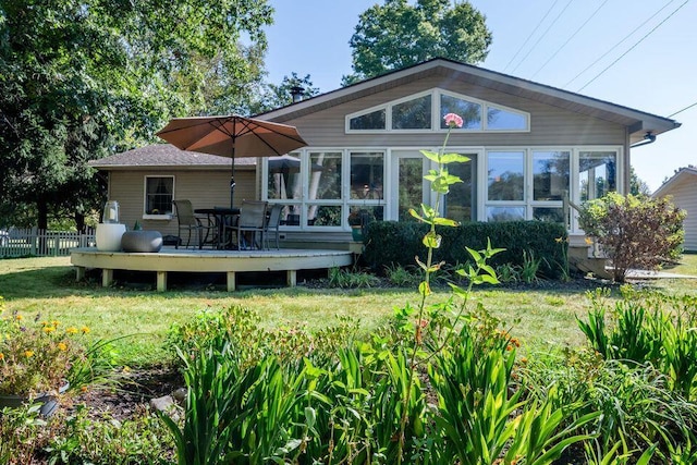 rear view of property featuring a sunroom, a lawn, a wooden deck, and fence